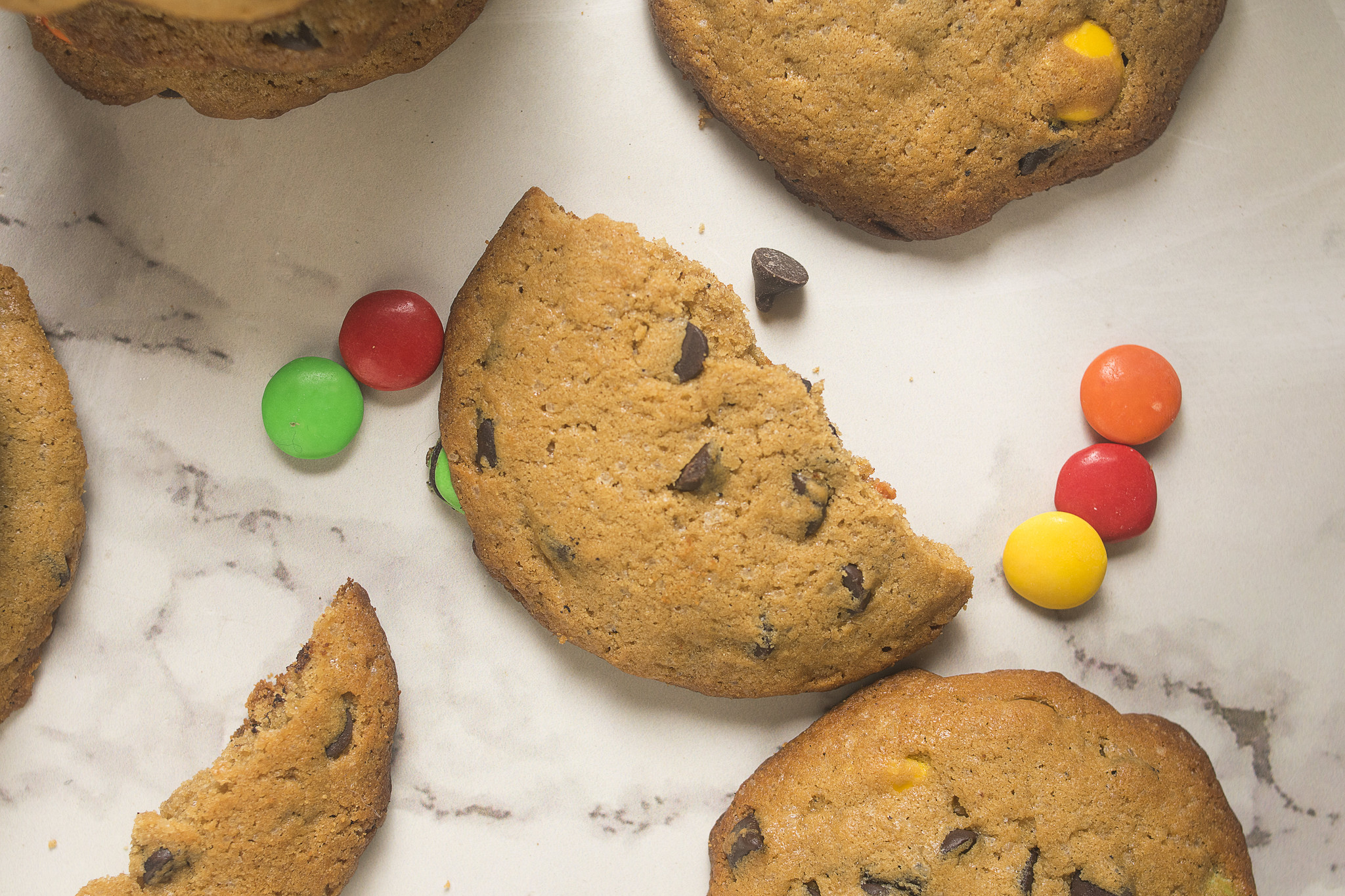 Overhead view of browned butter chocolate chip cookies with one cookie broken open and colourful M&Ms scattered around.